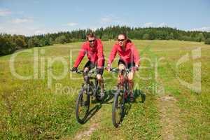 Young couple riding mountain bike in spring meadow
