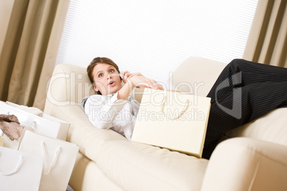 Young business woman lying down on sofa with shopping bag