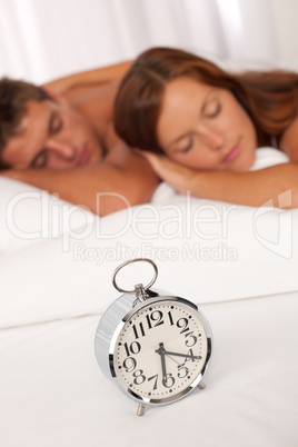 Young couple lying in white bed with alarm clock