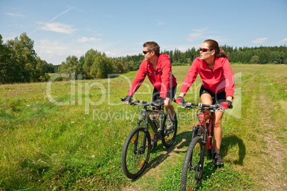 Young couple riding mountain bike in spring meadow