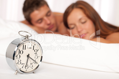 Young couple lying in white bed with alarm clock