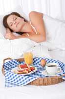 Woman sleeping in white bed, breakfast in foreground