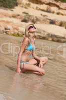 Blond fashion model sunbathing in bikini on beach