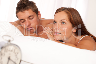 Young couple lying in white bed with alarm clock