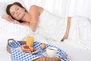 Woman sleeping in white bed, breakfast in foreground