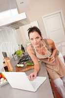 Woman with glass of white wine and laptop in the kitchen
