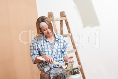 Home improvement: Smiling woman with paint and brush painting wa