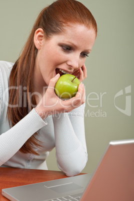Long red hair woman biting apple at office