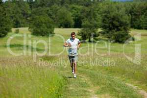 Young man with headphones jogging in a meadow