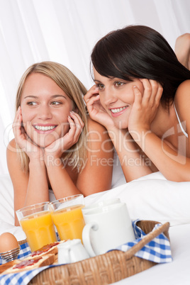 Two smiling women lying down in bed having breakfast