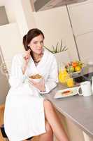 Happy woman eating cereals for breakfast in kitchen