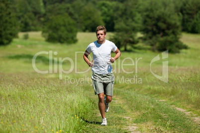 Young man with headphones jogging in a meadow