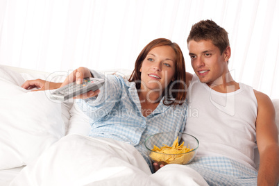 Young woman and man lying in bed watching television