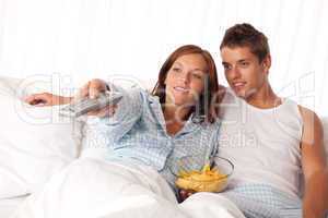 Young woman and man lying in bed watching television