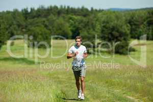 Young man with headphones jogging in a meadow