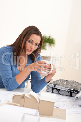 Brown hair female architect sitting at office holding coffee