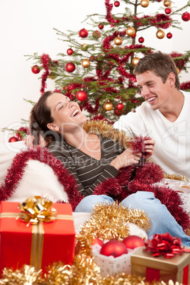 Young couple sitting together in front of Christmas tree
