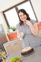 Happy plus size woman with chocolate cake and cream in kitchen