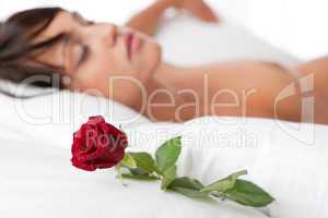 Woman lying in white bed, focus on rose