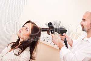 Professional hairdresser with hair dryer at salon with customer