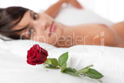 Woman lying in white bed, focus on rose