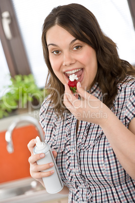 Plus size woman with whipped cream on strawberry in kitchen