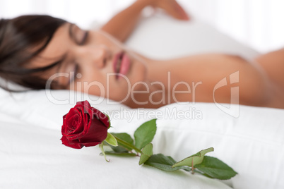 Woman lying in white bed, focus on rose