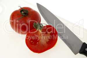Cutting white plastic board with a knife and tomato