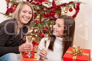 Two young woman with champagne and Christmas tree