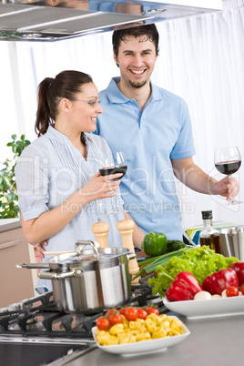 Smiling couple drink red wine cooking in kitchen