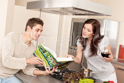 Young couple in kitchen choosing recipe from cookbook