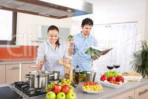 Young happy couple cook in kitchen with cookbook