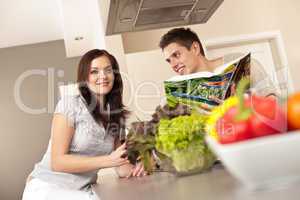 Young couple in kitchen choosing recipe from cookbook