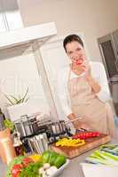 Smiling happy woman biting red pepper in the kitchen