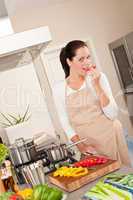 Happy woman biting red pepper in the kitchen