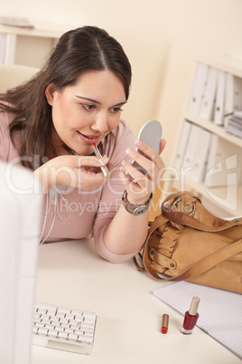 Young executive woman applying lipstick at office