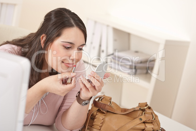 Young executive woman applying lipstick at office