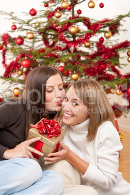 Two smiling women with Christmas present kissing
