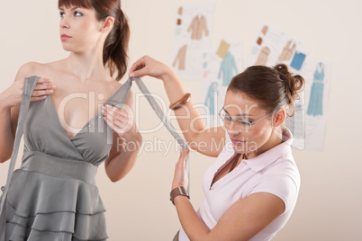 Female fashion designer pinning gray dress on model