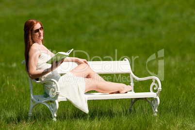 Red hair woman reading book on white bench in spring