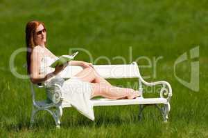 Red hair woman reading book on white bench in spring