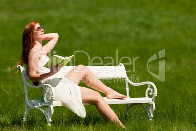 Red hair woman reading book on white bench in spring