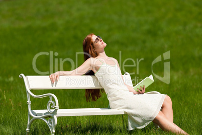 Red hair woman relaxing with book on white bench in spring