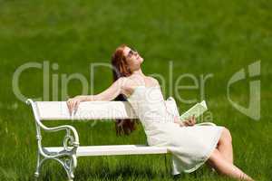 Red hair woman relaxing with book on white bench in spring