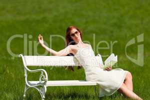 Red hair woman sitting on white bench in spring