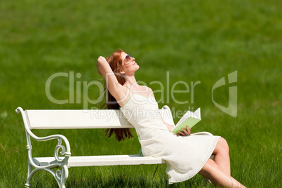 Red hair woman enjoying sun on white bench in spring