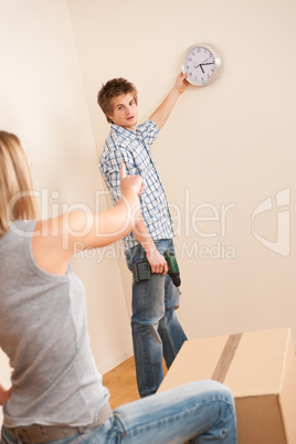 Moving house: Young couple hanging clock on wall