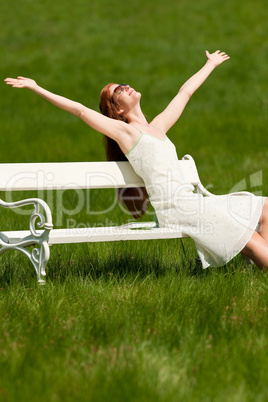 Red hair woman enjoying sun on white bench in spring