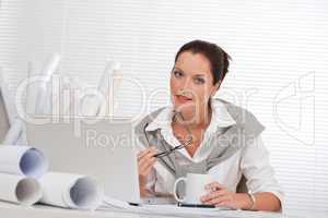 Smiling female architect with laptop and coffee sitting