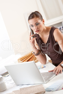 Young female designer on the phone at office with laptop